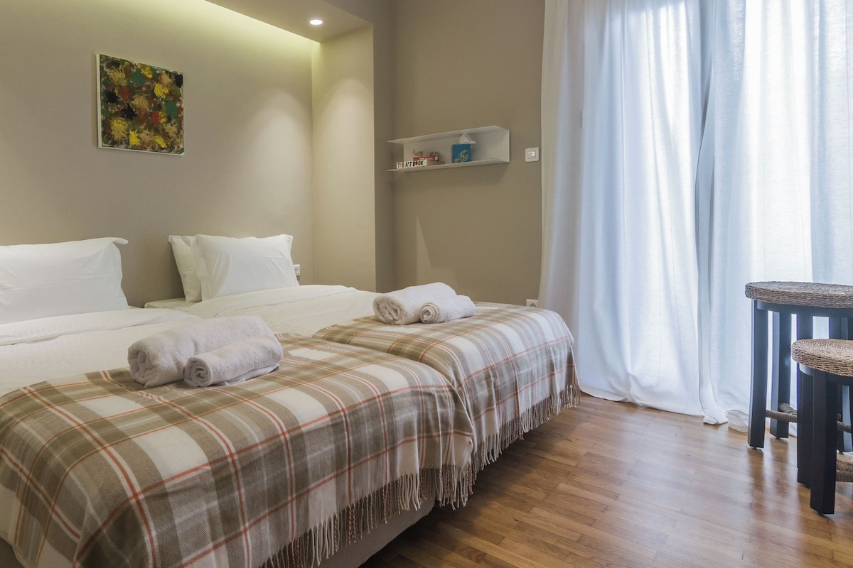 A hotel room with two beds, a plaid blanket, a small shelf with toiletries, and a cat tree.