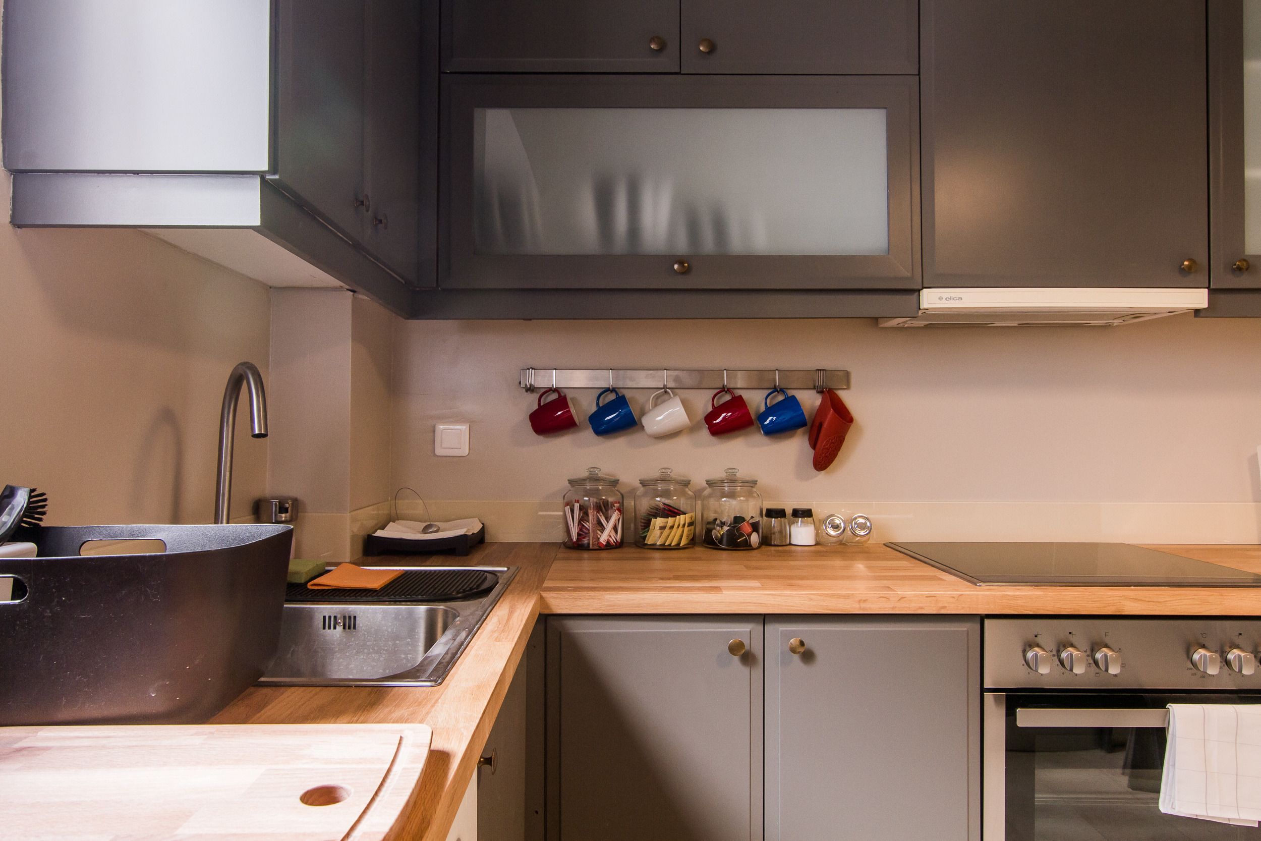 A modern kitchen with stainless steel appliances, a wooden countertop, and a variety of utensils and spices on the wall.