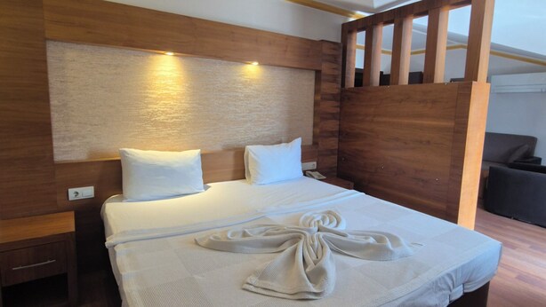 A modern hotel room with a large bed, wooden headboard, and a wooden partition. - Dinara Hotel (Kemer)