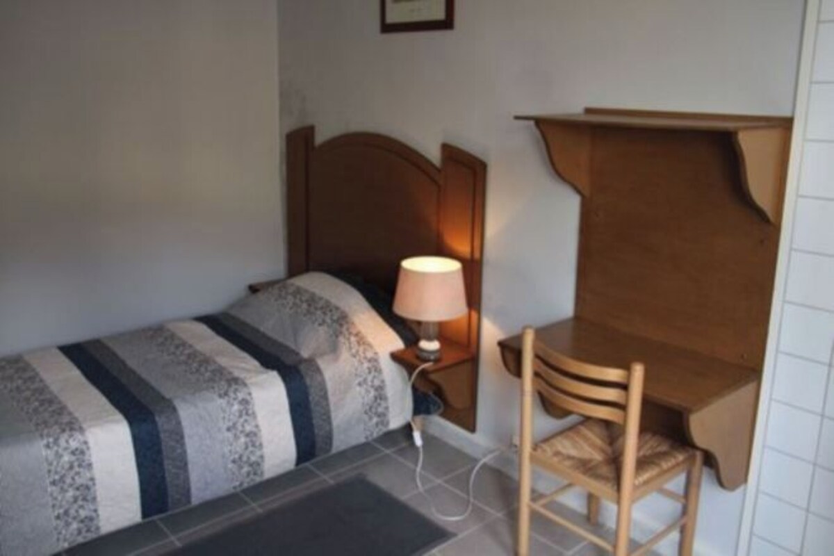 A single bed with a patterned bedspread, a bedside table with a lamp, and a wooden chair.