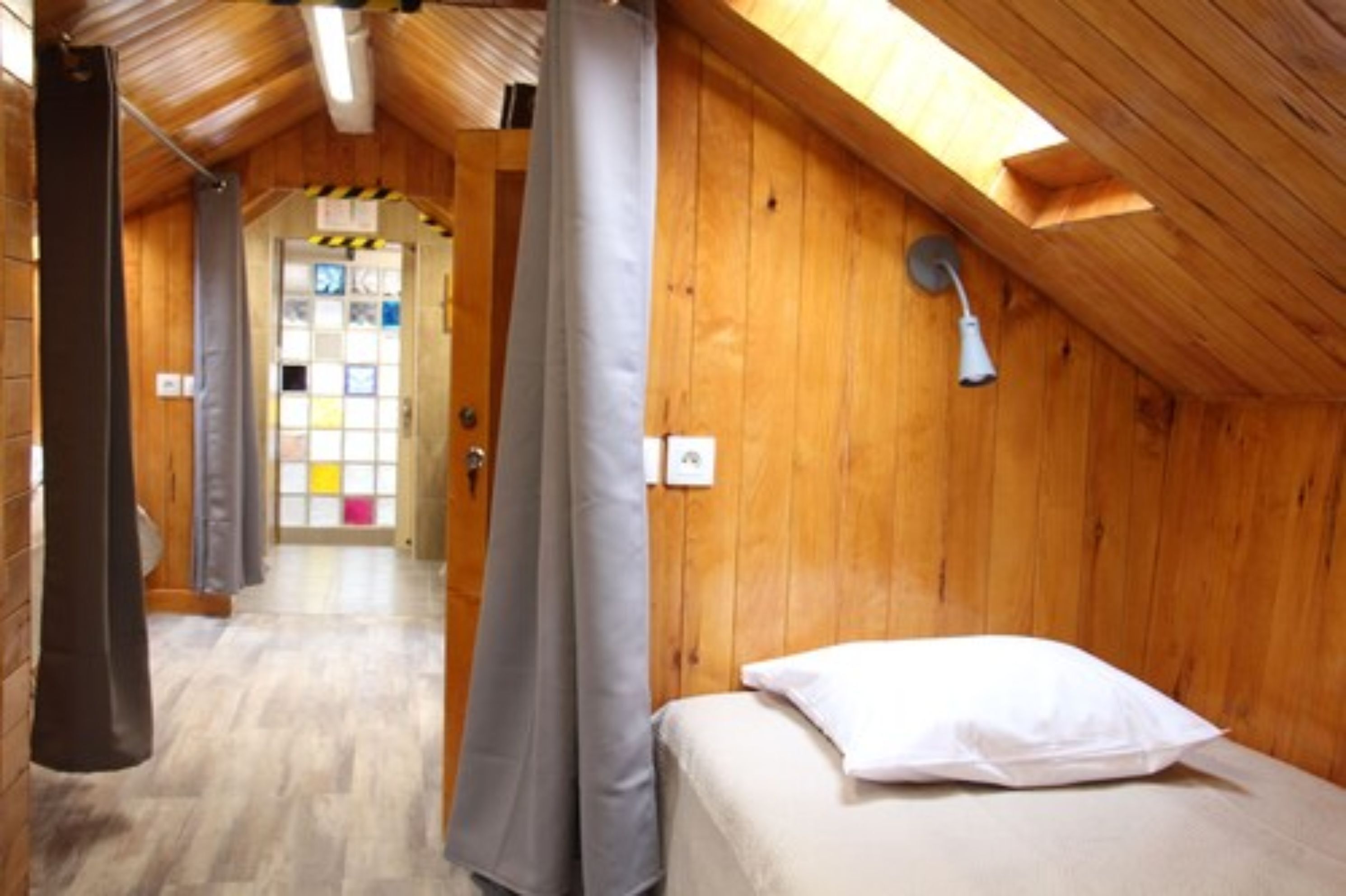 Una habitación con paneles de madera, una cama, una ventana y una puerta que da a otra estancia.