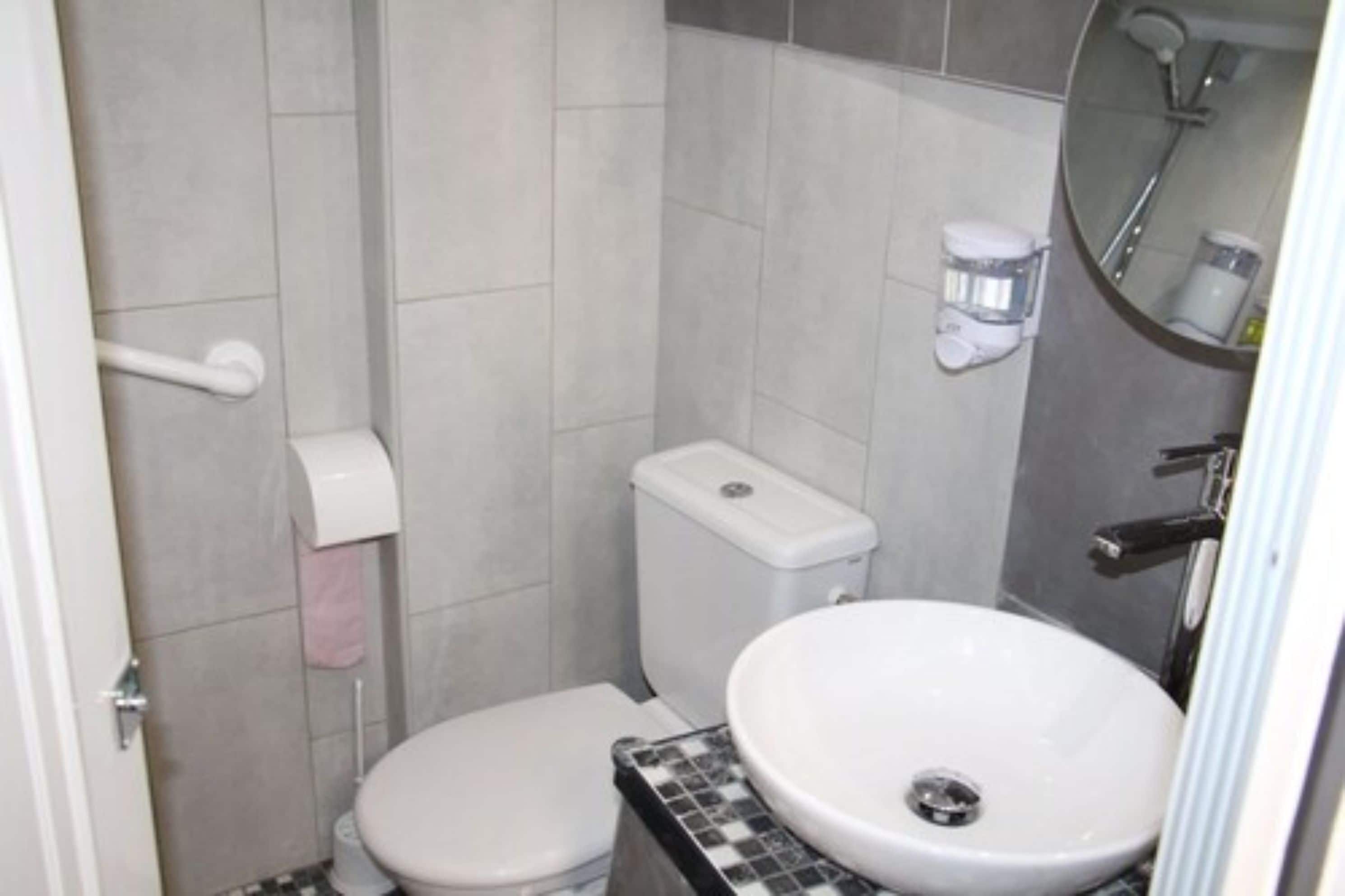 A small bathroom with a toilet, sink, and a mirror.
