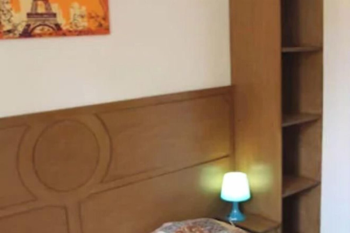 A room with a wooden headboard, a lamp on a bedside table, and a painting of the Eiffel Tower.
