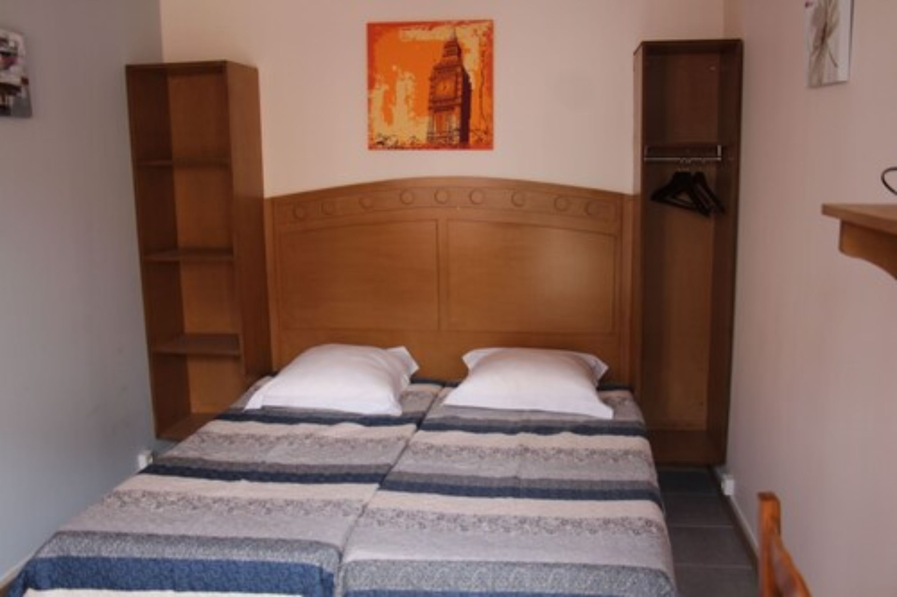 A single bed with a wooden headboard, two bedside tables, and a painting of a tower on the wall.