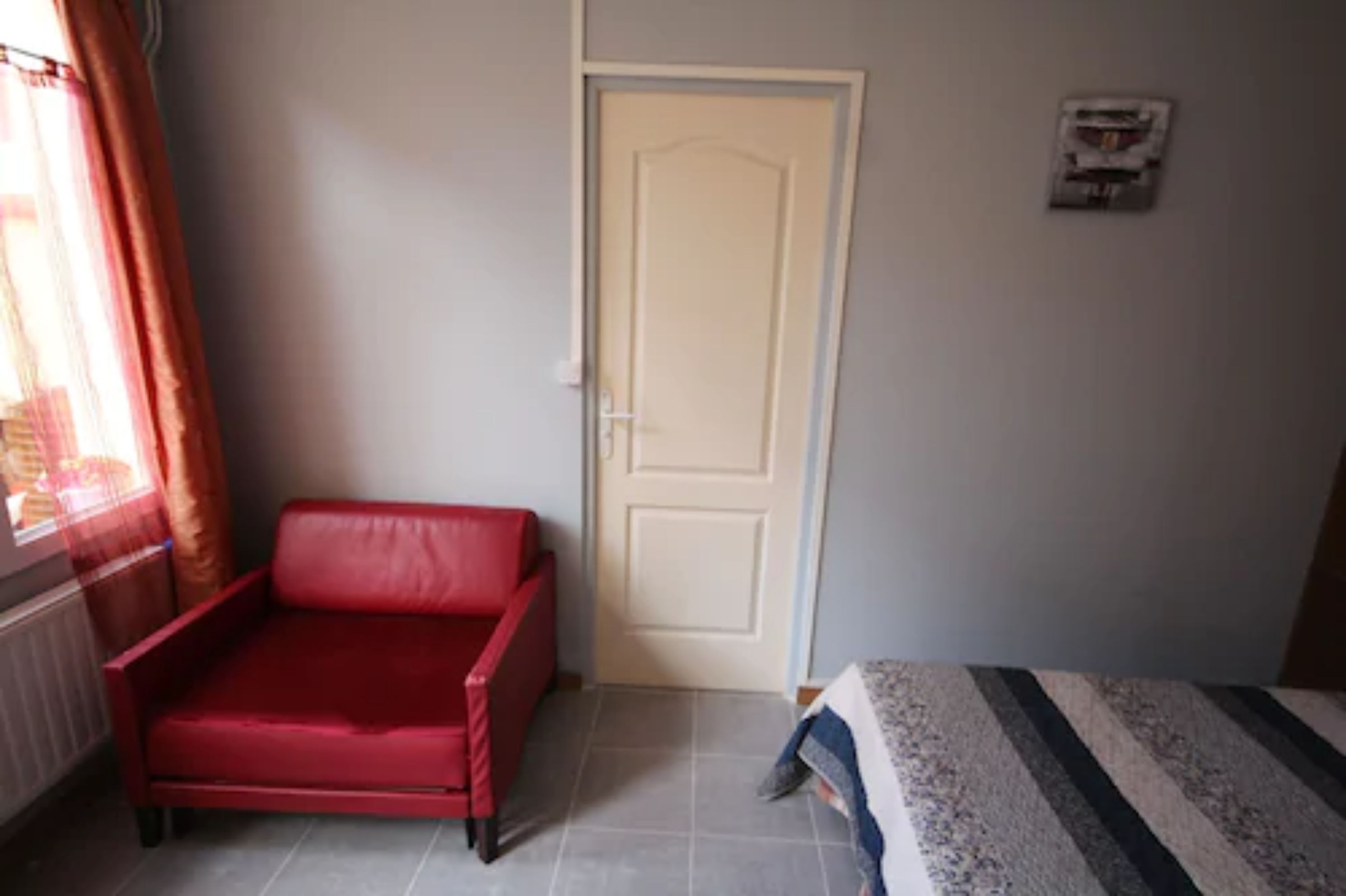 A room with a red sofa, a white door, and a bed with striped bedding.