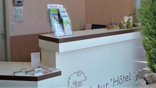A reception desk with brochures, a wall-mounted information board, and a small basket with decorative items. - Natur'Hôtel (Menesplet)