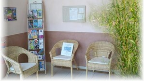 A reception area with wicker chairs, a bulletin board with pamphlets, and a wall-mounted light fixture. - Natur'Hôtel (Menesplet)