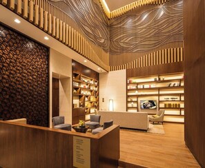 A hotel lobby with a reception desk, seating area, and bookshelves. - Ascott Central Wuxi (Wuxi)