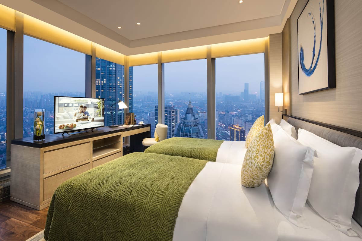 Ein modernes Hotelzimmer mit einem großen Bett, einem Schreibtisch mit Fernseher und Blick auf die Stadt.