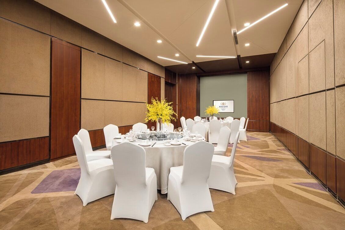 Uma sala de conferências com mesas redondas, cadeiras brancas e um arranjo floral.