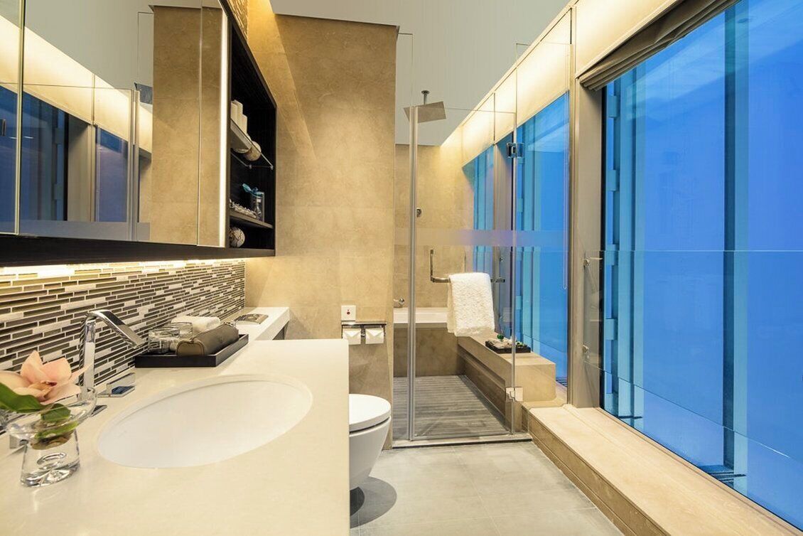 Une salle de bain moderne avec un grand lavabo, une douche en verre et une vue dégagée sur l’extérieur grâce à une grande fenêtre.