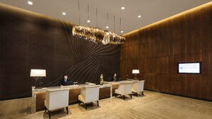 A reception area with a modern design, featuring a reception desk, several chairs, and a large, abstract light fixture. - Ascott Central Wuxi (Wuxi)