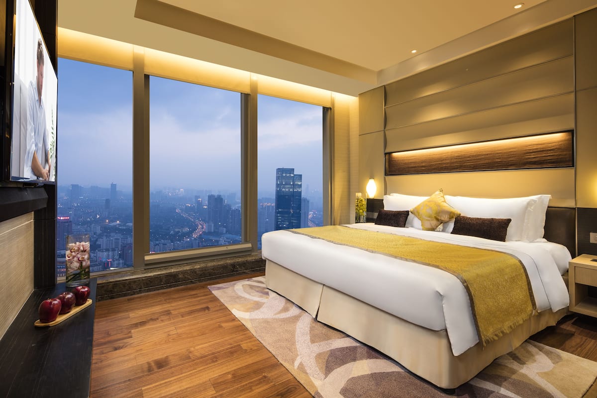 Ein modernes Schlafzimmer mit einem großen Bett, einem Nachttisch und Blick auf die Stadt durch große Fenster.