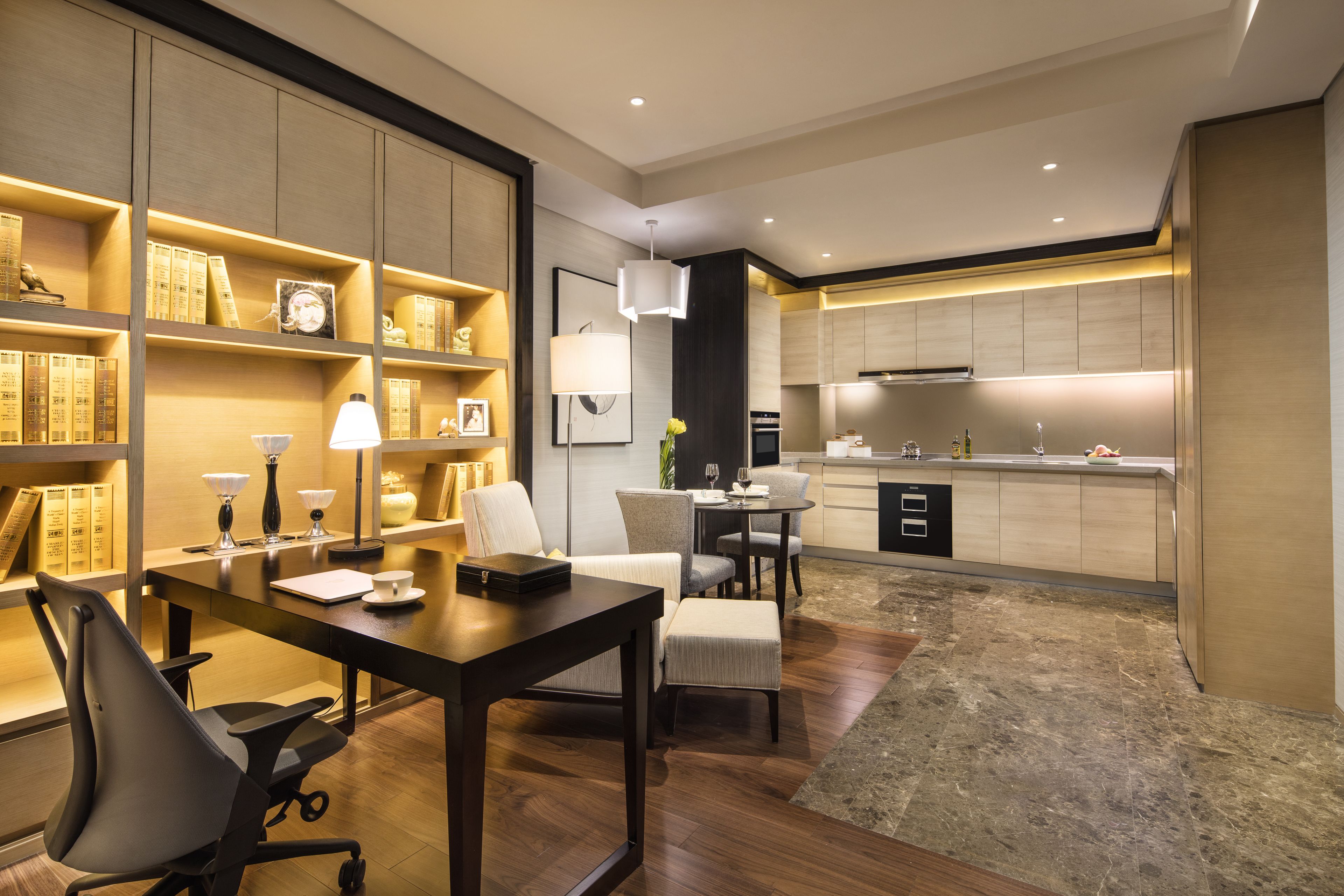 A modern kitchen with built-in appliances, a dining area with a table and chairs, and a bookshelf with decorative items.