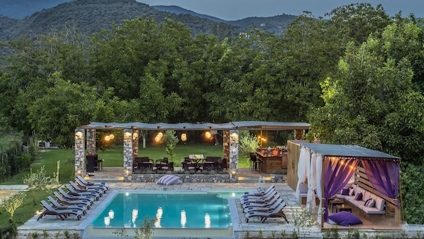 Un área junto a la piscina con sillones de descanso, un pabellón de piedra y una zona de estar cubierta con bar.