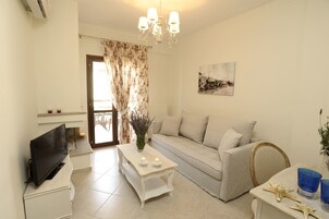 A living room with a sofa, a TV, a table with candles, and a chandelier.