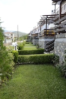 A residential area with stone walls, a well-maintained lawn, and a staircase leading to a balcony.