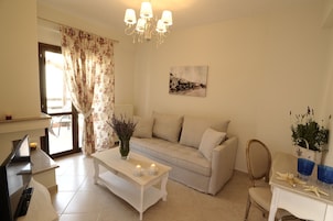 A living room with a sofa, a coffee table, a TV, and a chandelier.