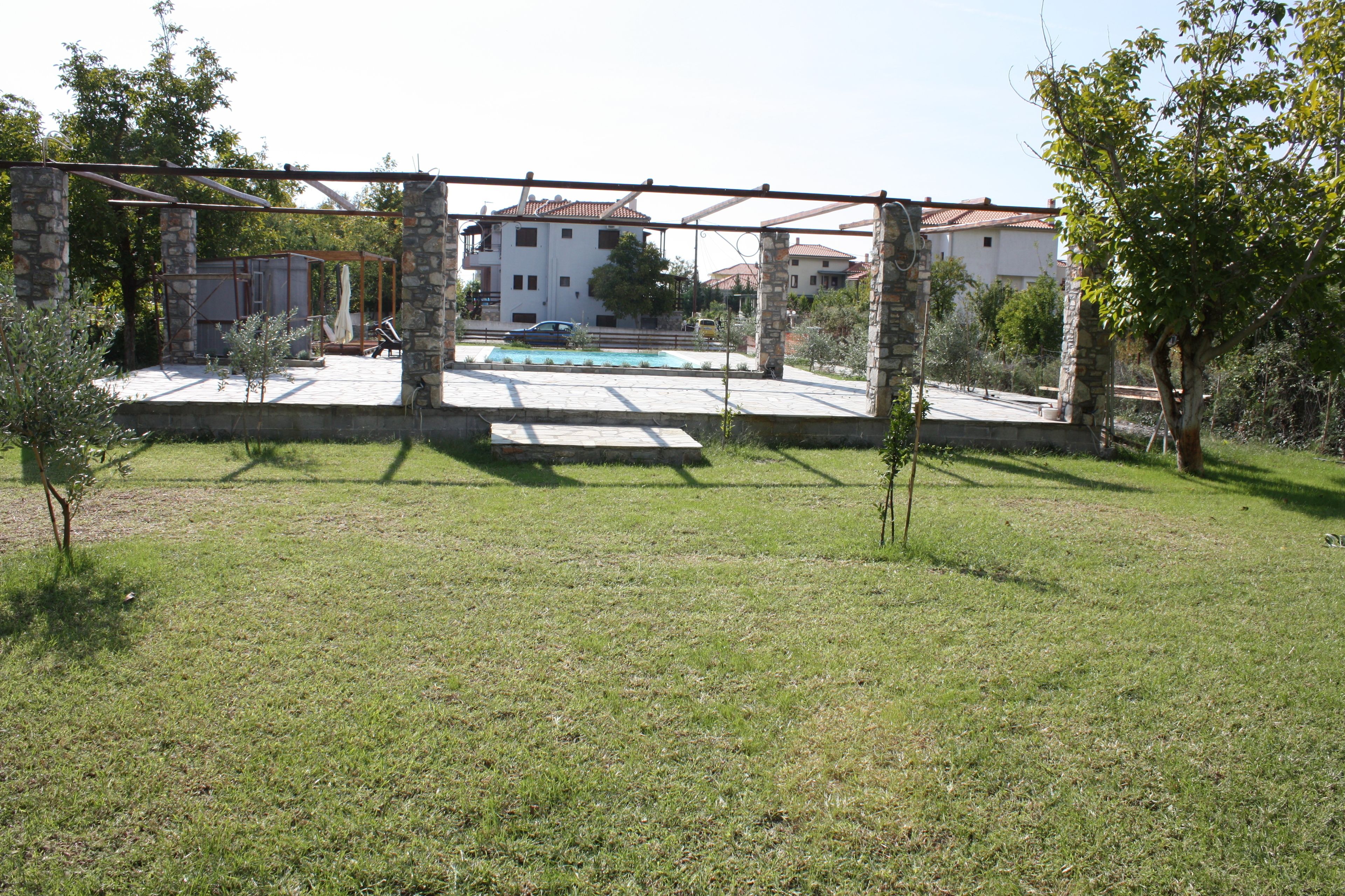 Uma área externa cercada com piscina, pilares de pedra e vista para edifícios residenciais ao fundo.