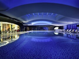 Una piscina interna moderna con parete in vetro, attrezzature per esercizi e poltrone relax.