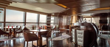 A spacious hotel lobby with high ceilings, large windows offering a city view, and modern furniture.