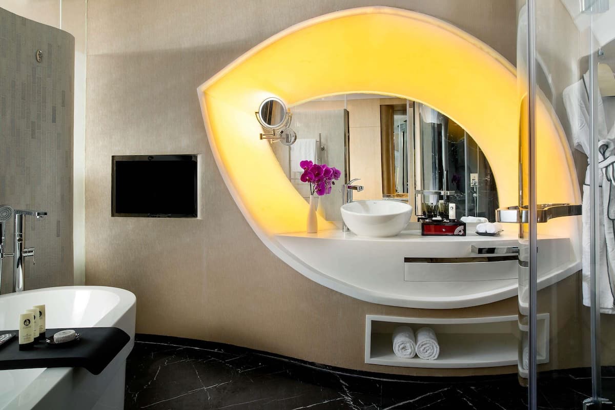 A modern bathroom with a freestanding bathtub, a large oval mirror, and a vanity with a sink and toiletries.