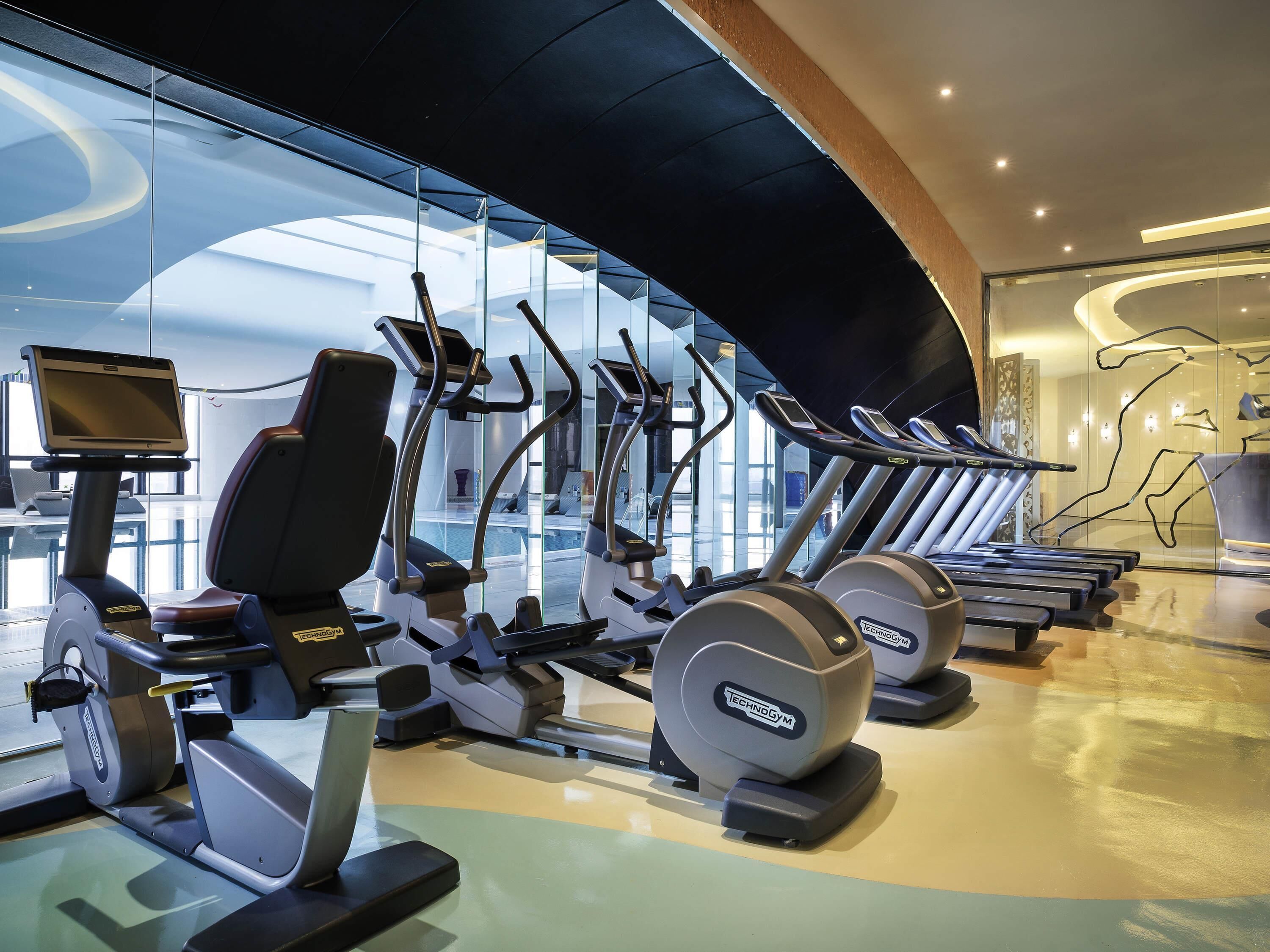 A gym with various exercise machines, a large glass wall, and a modern interior design.