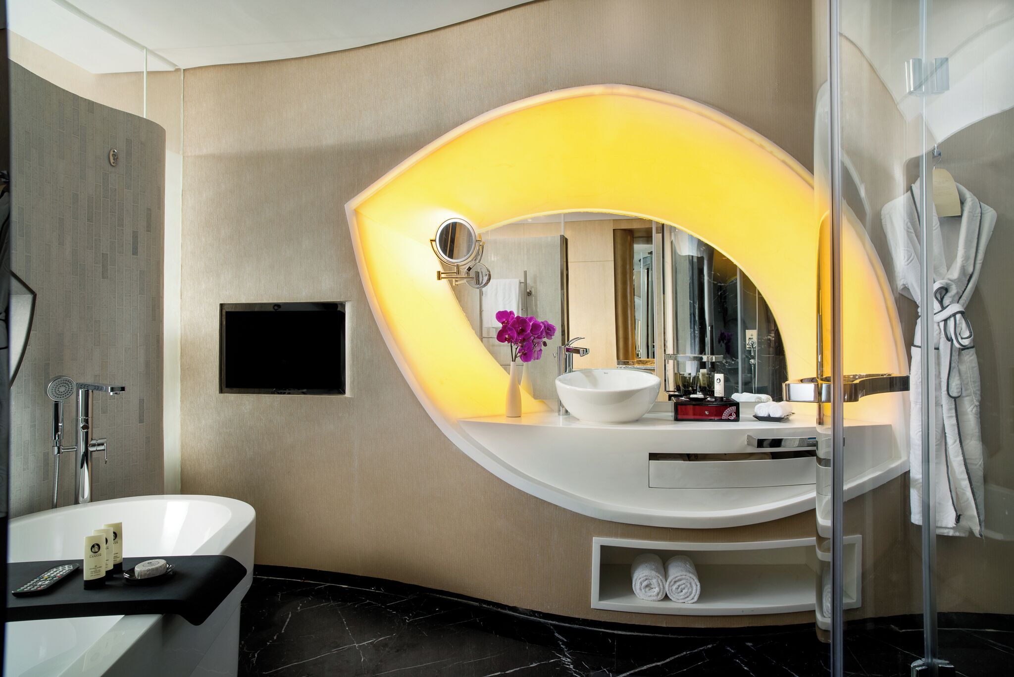 A modern bathroom with a freestanding bathtub, a large mirror with a yellow light, a white sink, and a glass shower enclosure.