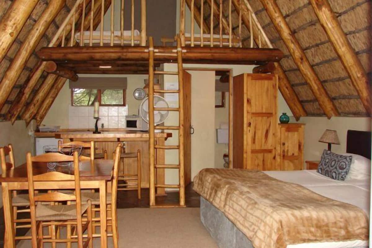 Een gezellig slaapkamer op zolder met een verhoogd keukenhoekje, houten meubels en een bed met een geborduurd beddegoed.