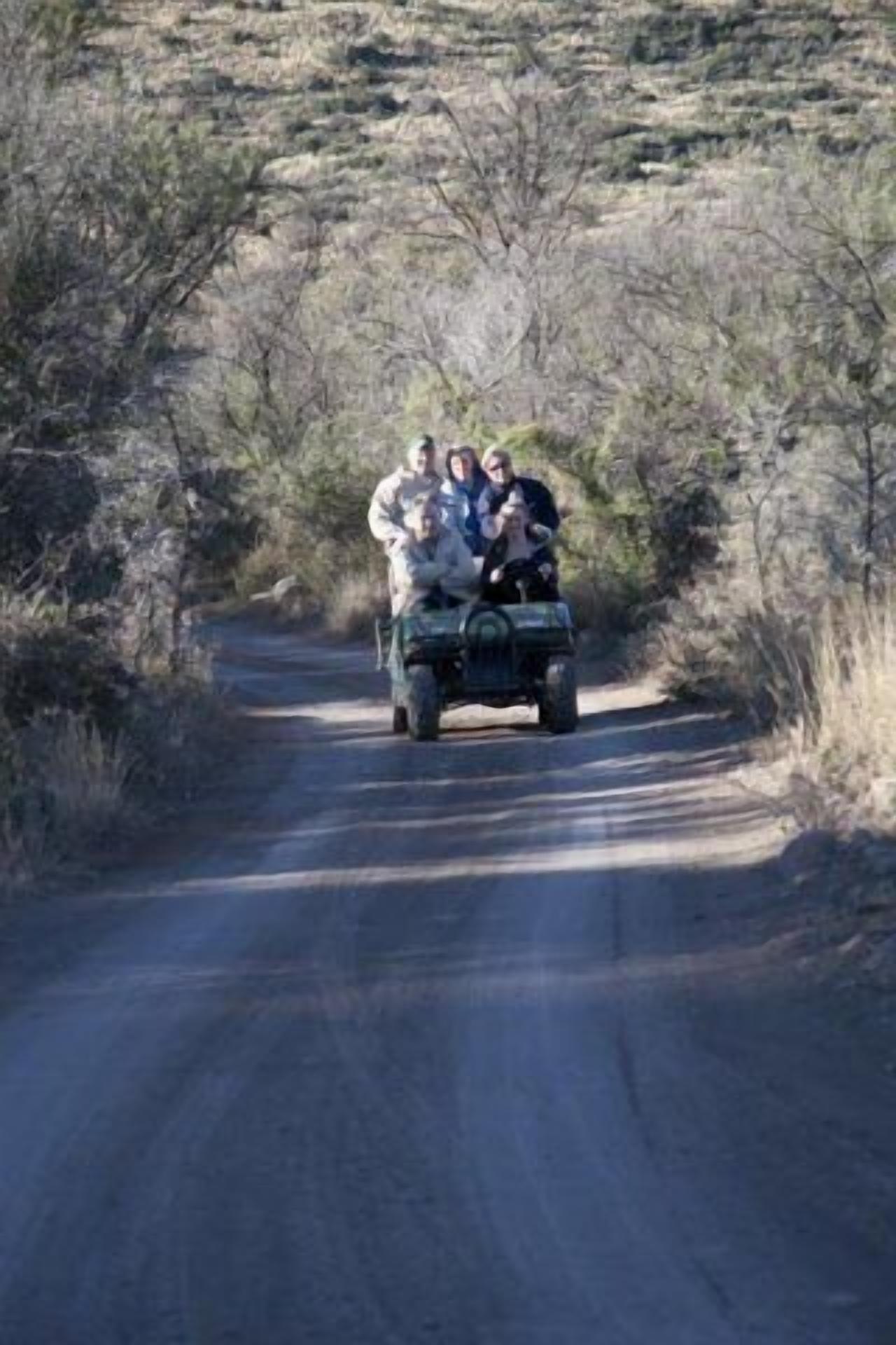 Un grupo de personas en un vehículo por un camino rural, rodeado de vegetación escasa.