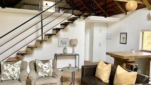 Amplia sala de estar con escaleras, un conjunto de sofás, una mesa de comedor y una zona de cocina.