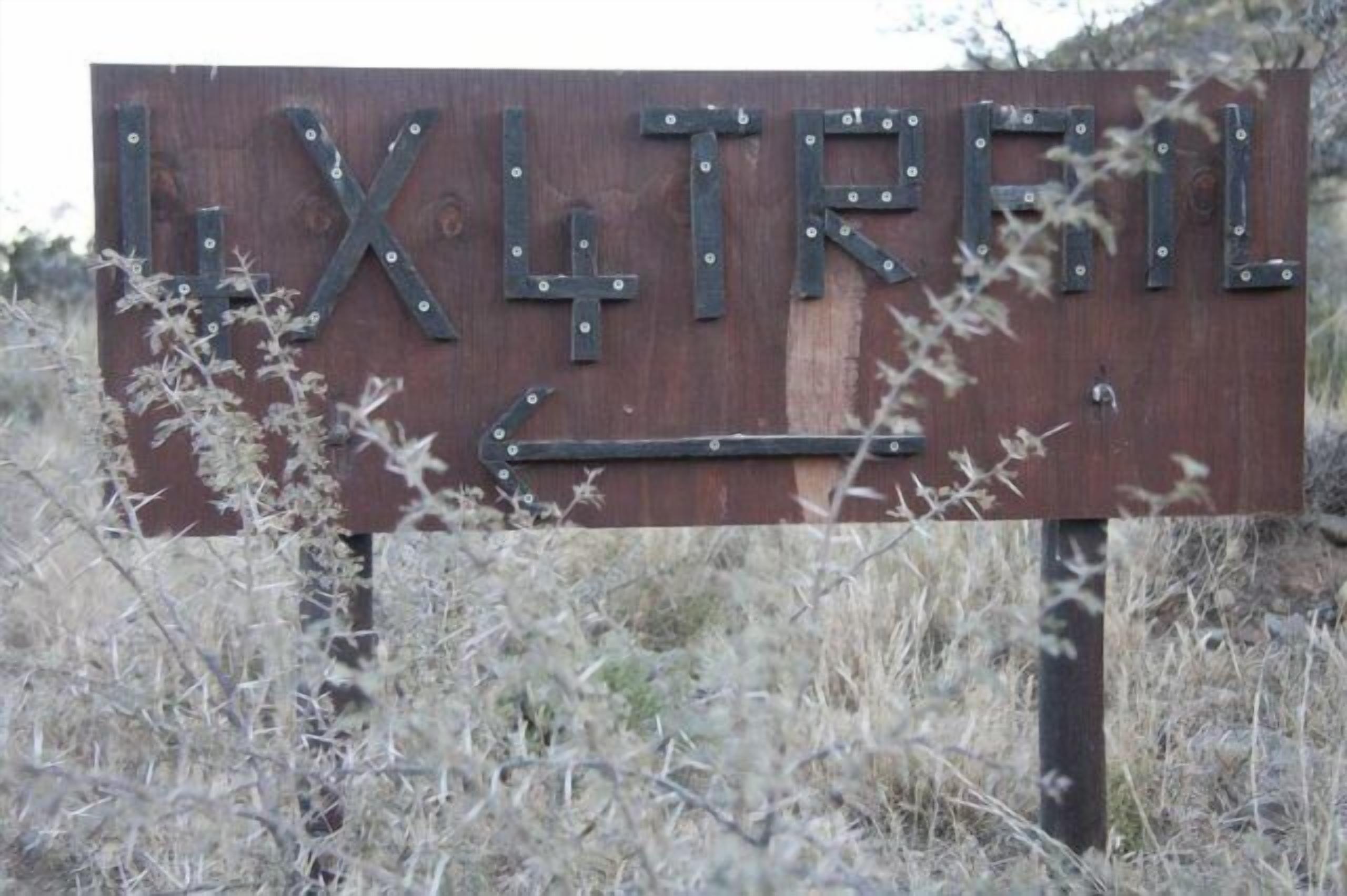 Ein Holzschild mit der Aufschrift 'LXT TRFIL', befestigt an einem Metallpfosten.