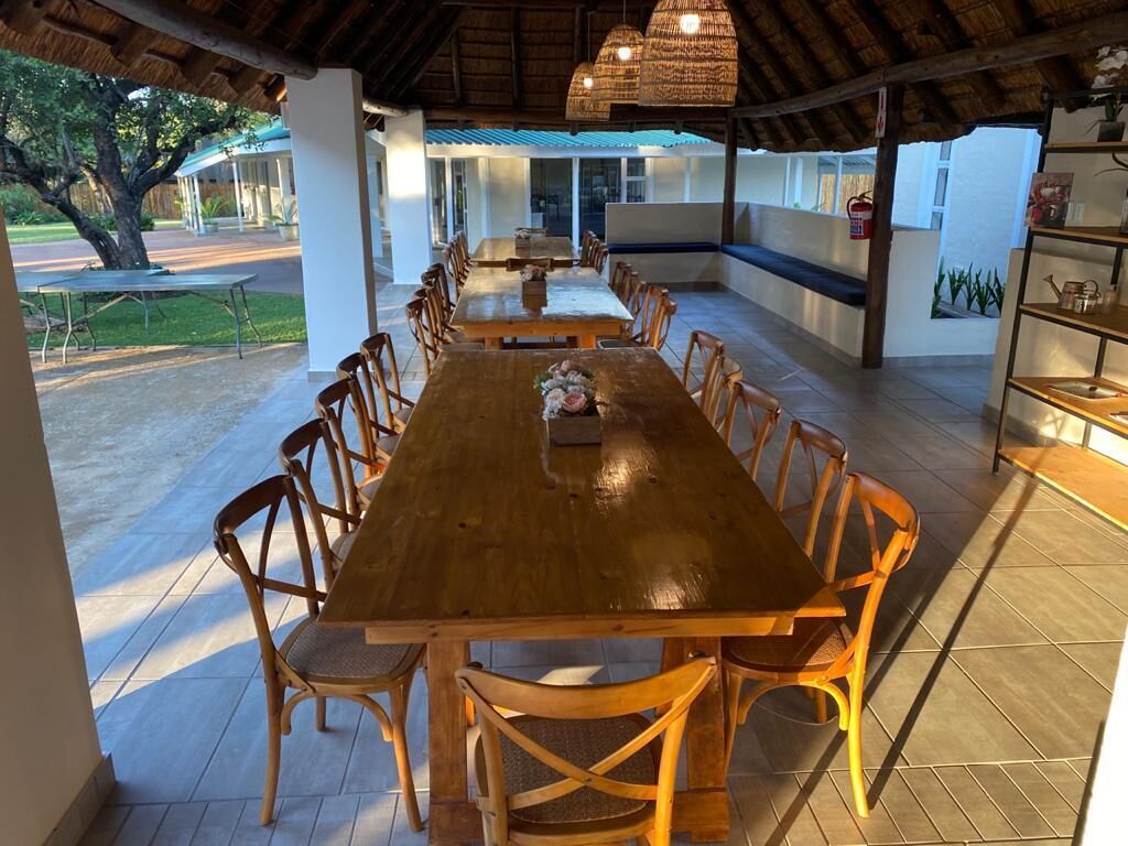 Un vaste espace extérieur aménagé pour les repas, avec une longue table en bois et des chaises, entouré d’une terrasse couverte dotée d’un toit de chaume.