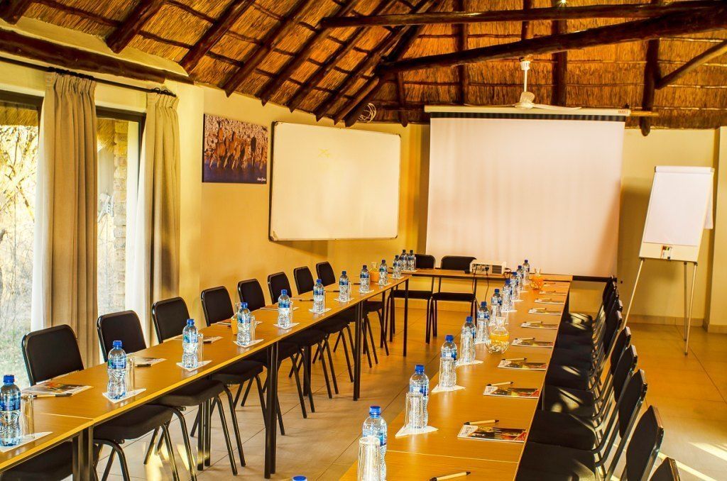Une salle de conférence équipée d’une longue table, de chaises, de bouteilles d’eau, d’un tableau blanc et d’un écran de projection.
