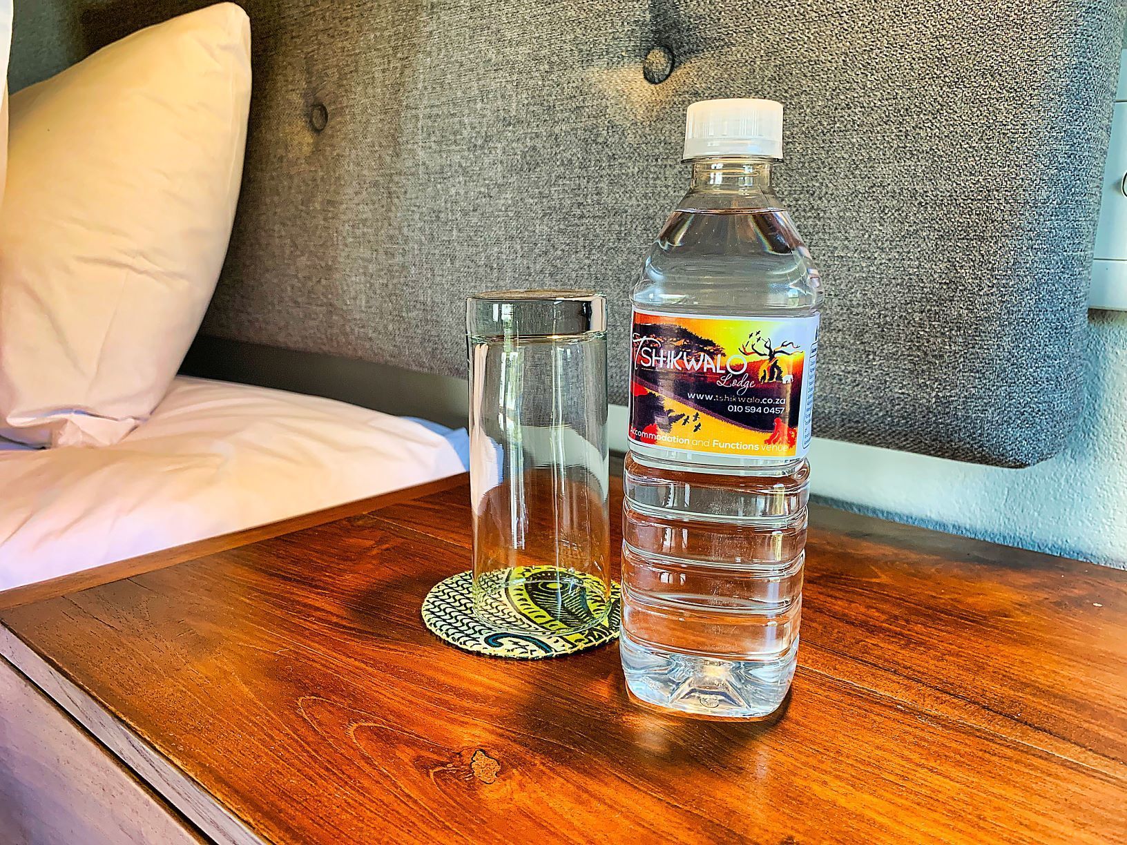 A bottle of water and a glass on a wooden table in a hotel room.