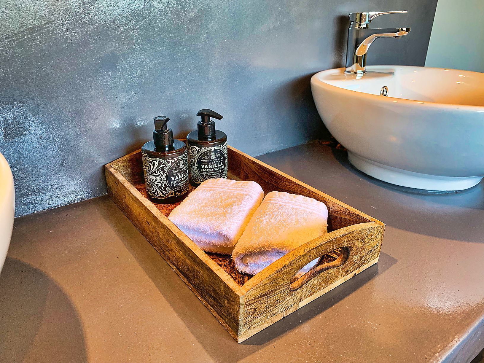 A wooden tray with two towels and two body care bottles on a bathroom counter.