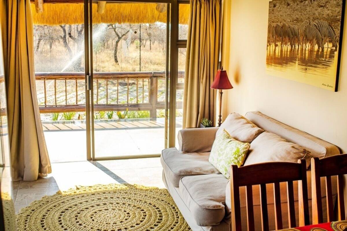 Una habitación con sofá, lámpara y un ventanal con cortinas.