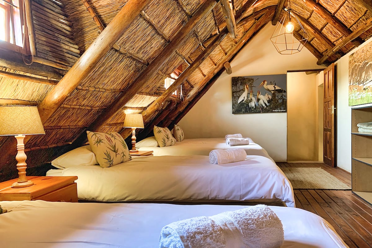 Una habitación con dos camas, techo de madera, un cuadro de pájaros y un armario de madera.