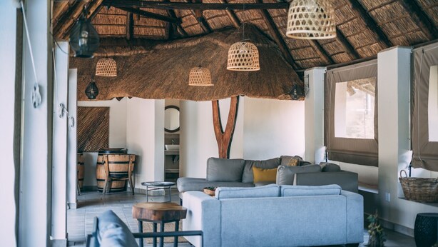Amplia sala de estar con techo de paja, un conjunto de sofás, comedor y vistas a través de una ventana.