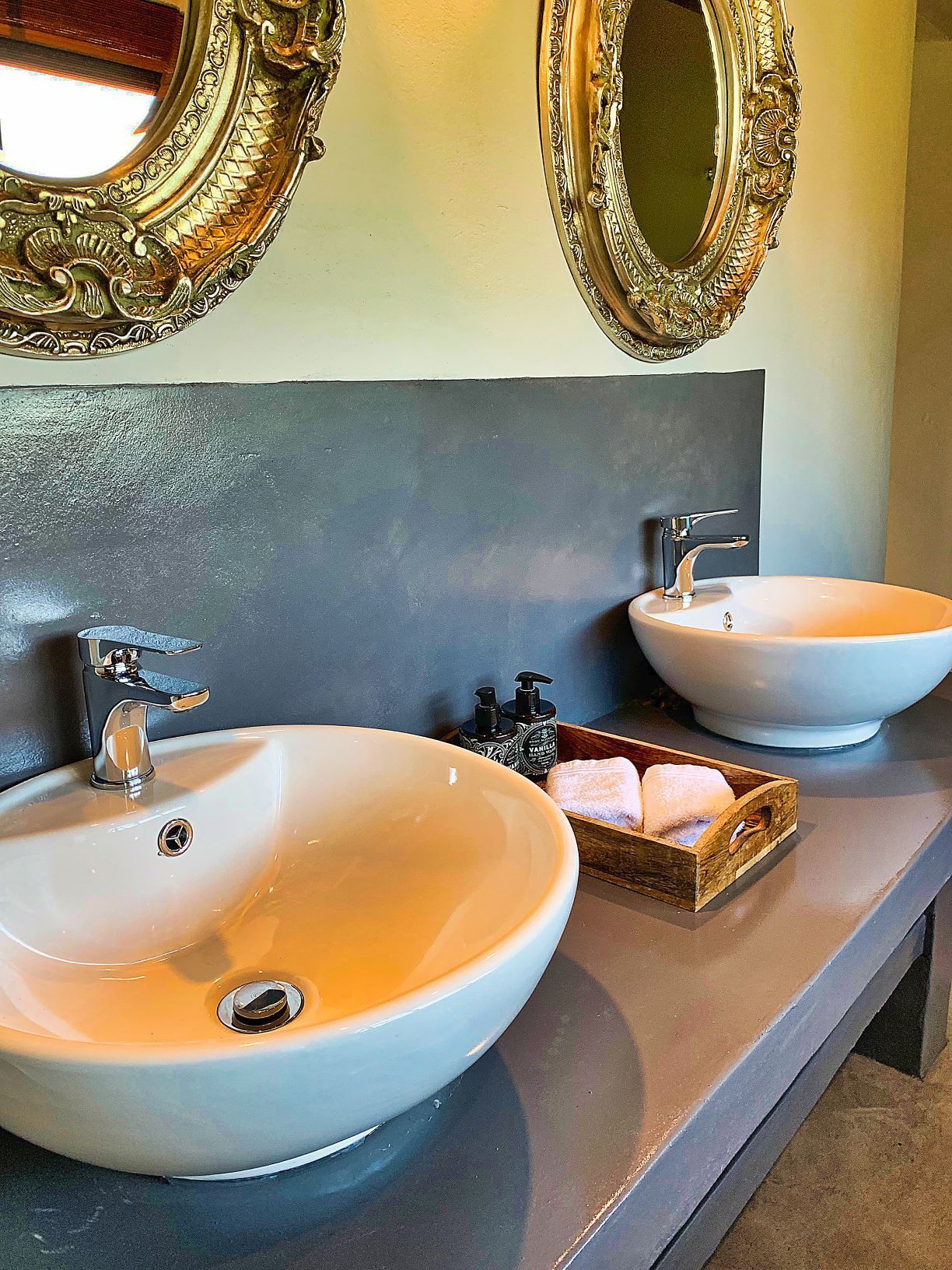 A bathroom with two white sinks, a dark countertop, and two ornate mirrors.