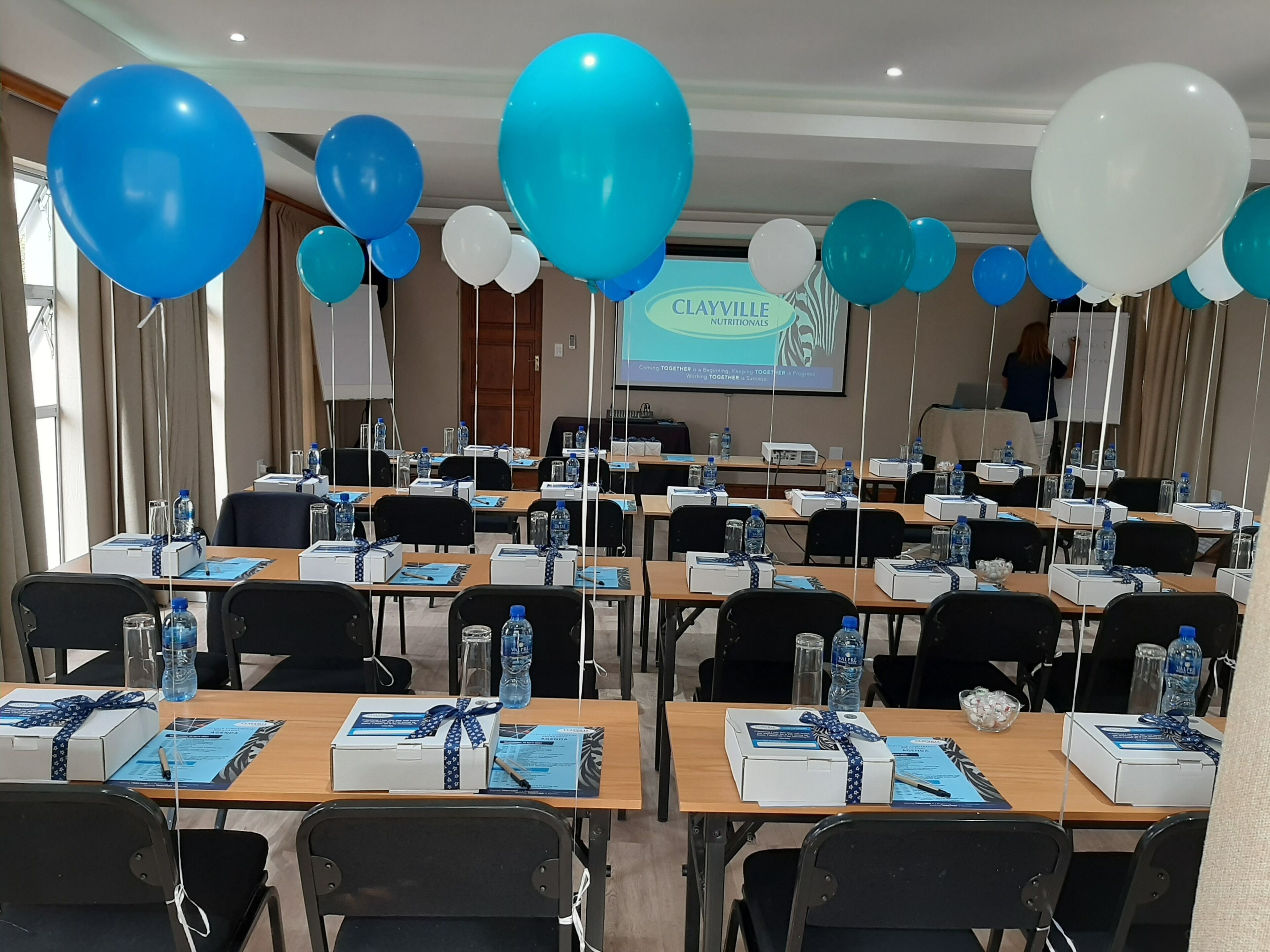 Ein Konferenzraum mit für eine Besprechung gedeckten Tischen, Luftballons und einer Präsentationsleinwand.