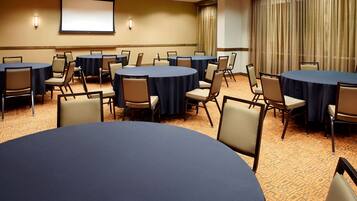 A conference room with multiple round tables, chairs, a projector screen, and a large window with curtains.
