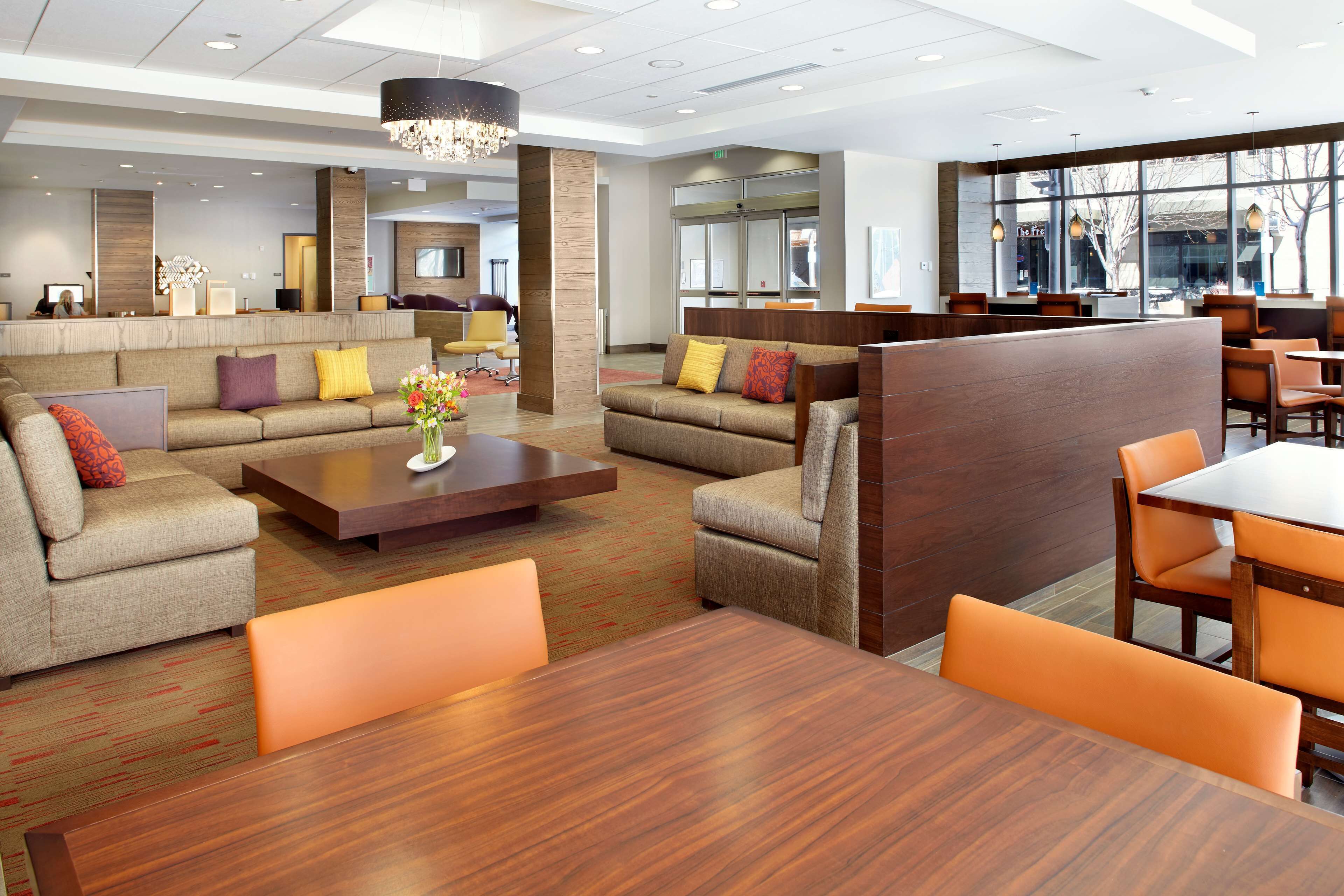 A modern hotel lobby with sofas, a coffee table, and a dining area.