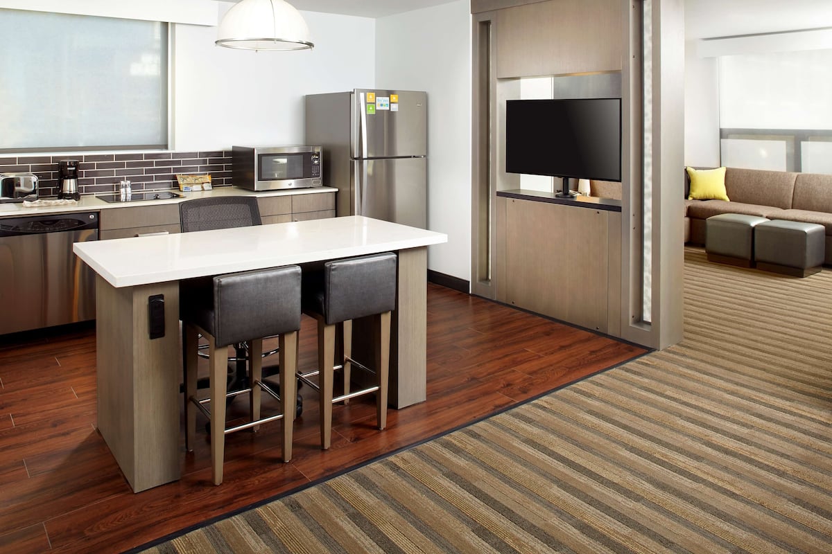 Una cocina moderna con encimera blanca, electrodomésticos de acero inoxidable y una zona de bar con taburetes.