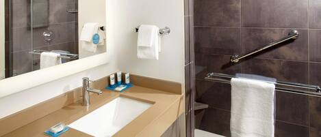 Un baño moderno con encimera color crema, lavabo blanco, espejo y cabina de ducha con paredes de vidrio.