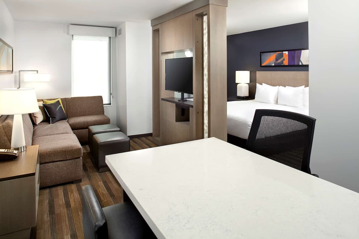 Habitación de hotel con una cama grande, televisión, escritorio con lámpara, sofá y mesa de comedor.