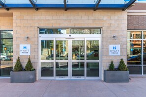 Entrada de hotel con puertas dobles, dos plantas en macetas y un letrero que indica que es un Hyatt House.