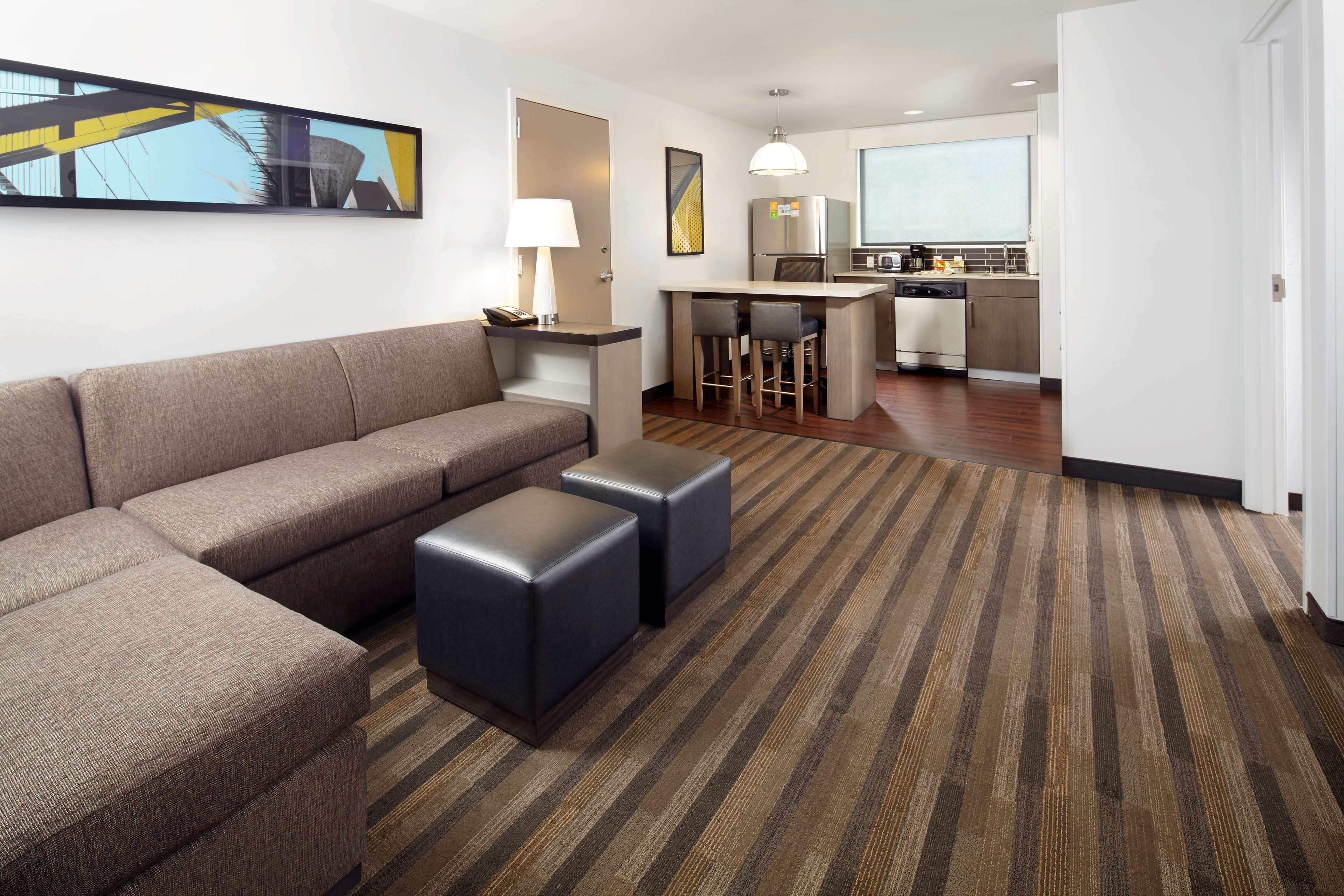 Una habitación de hotel moderna con sofá modular, pequeña cocina y alfombra a rayas.