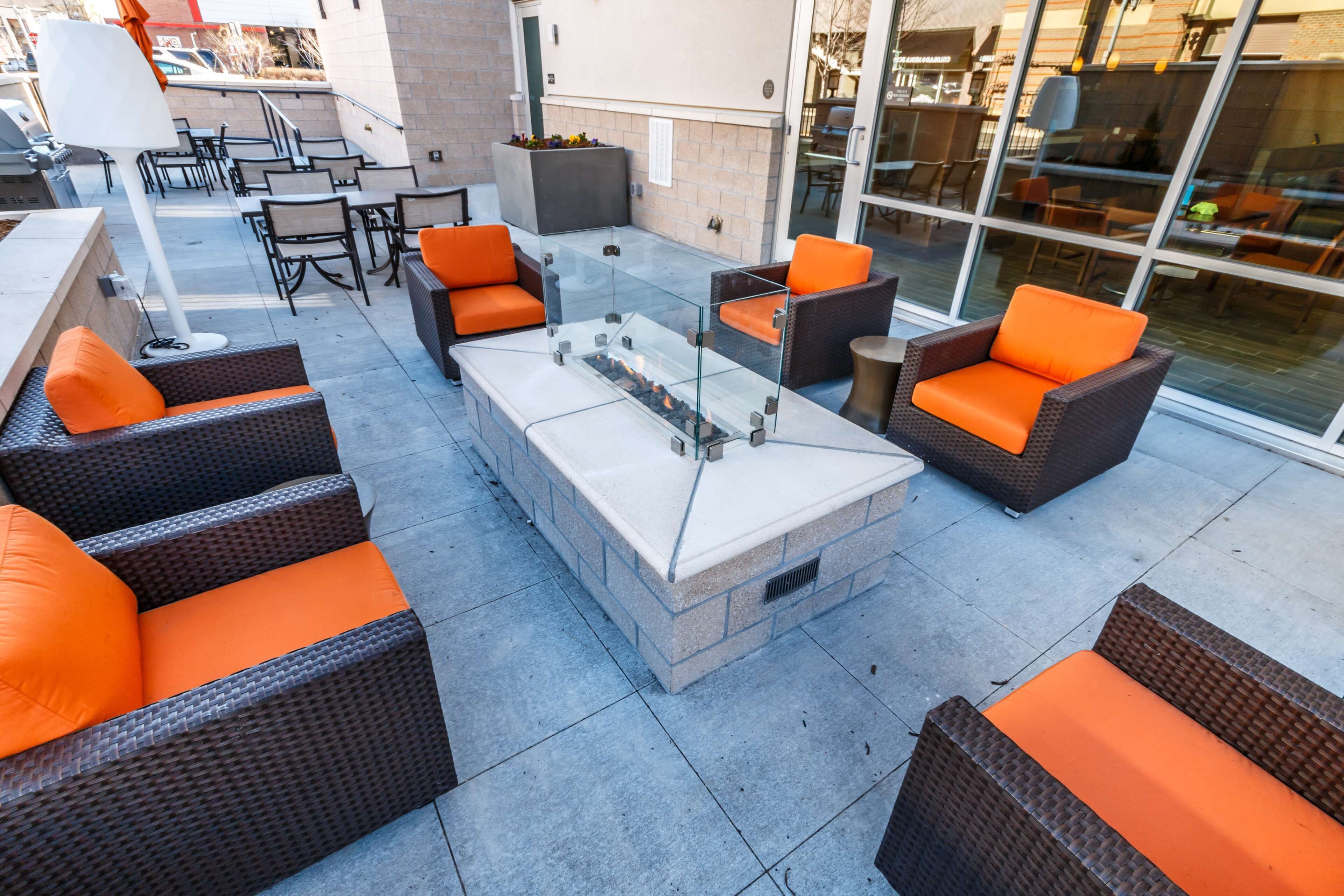 An outdoor patio area with wicker furniture, a glass-top table, and a built-in fire feature.