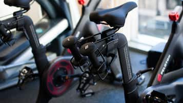A stationary bike with a red light on the wheel, a black seat, and a handlebar with a red button.